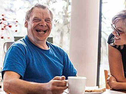 man laughing whilst drinking a coffee