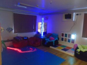 A photograph of the sensory room at Welland House: with fibre optic lights, a bubble tube, beanbags to sit on, and a colour and light board on the wall.