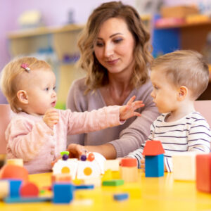 Little girl and boy preschoolers playing with teacher.