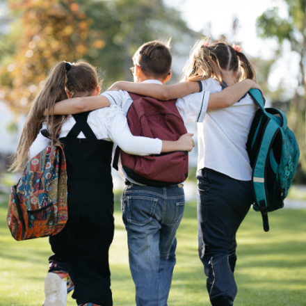 school friends a boy and two girls with school backpacks on their backs walk after class