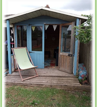 A wooden summer house with blue doors, bunting hanging on the front of it, and a deckchair outside.