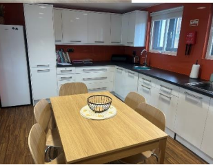 A kitchen with white cupboards and a black worktop, with a wooden dining table and chairs in the centre.