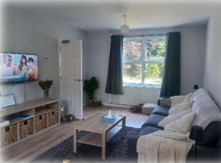 A lounge with sofa, coffee table, storage unit and a TV on the wall.