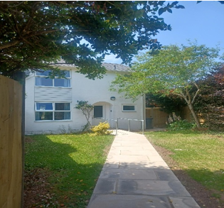 A white house with a grass lined path leading up to it.