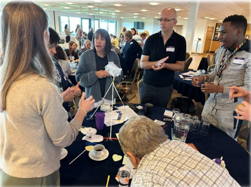 A group of adults standing around a table, carrying out a group activity.