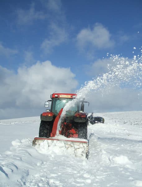 tractor in field covered in snow trying to clear snow