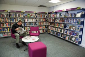 man sat in a library surrounded by books reading a paper