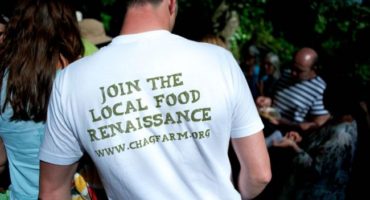 group of people gathered, man stood with back to camera wearing a white t-shirt that says join the local food renaissance www.chagfarm.org