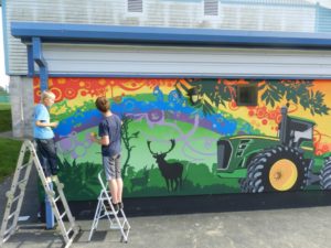 two young people stood on ladders next to green tractor mural on a colourful background