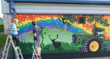 two young people stood on ladders next to green tractor mural on a colourful background