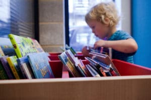 young child looking through a selection of books at library