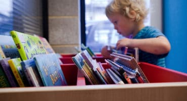 young child looking through a selection of books at library