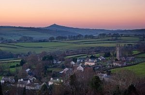 landscape photo of Peter Tavy village, houses, church, green fields and a pink sky