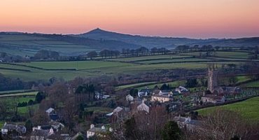 landscape photo of Peter Tavy village, houses, church, green fields and a pink sky