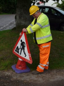 workman in hi vis putting up traffic cone with road works sign