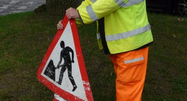 workman in hi vis putting up traffic cone with road works sign