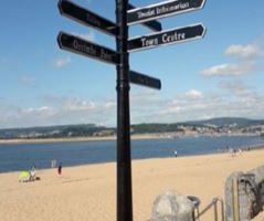 Black multi directional fingerpost sign on pavement next to the sandy beach at Exmouth