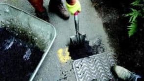 person filling in pothole using a spade on a road