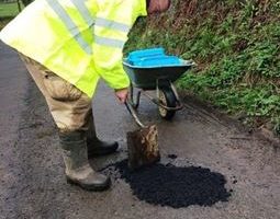 man in hi vis jacket with wheelbarrow and spade filling in pothole