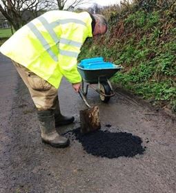 man in hi vis jacket with wheelbarrow and spade filling in pothole