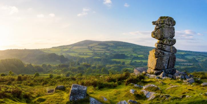 Haytor Rocks on Dartmoor overlooking green rolling countryside at sunset, with a large granite rock formation in the foreground.