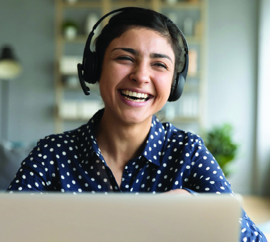 Woman laughing, sitting at a laptop wearing headphones