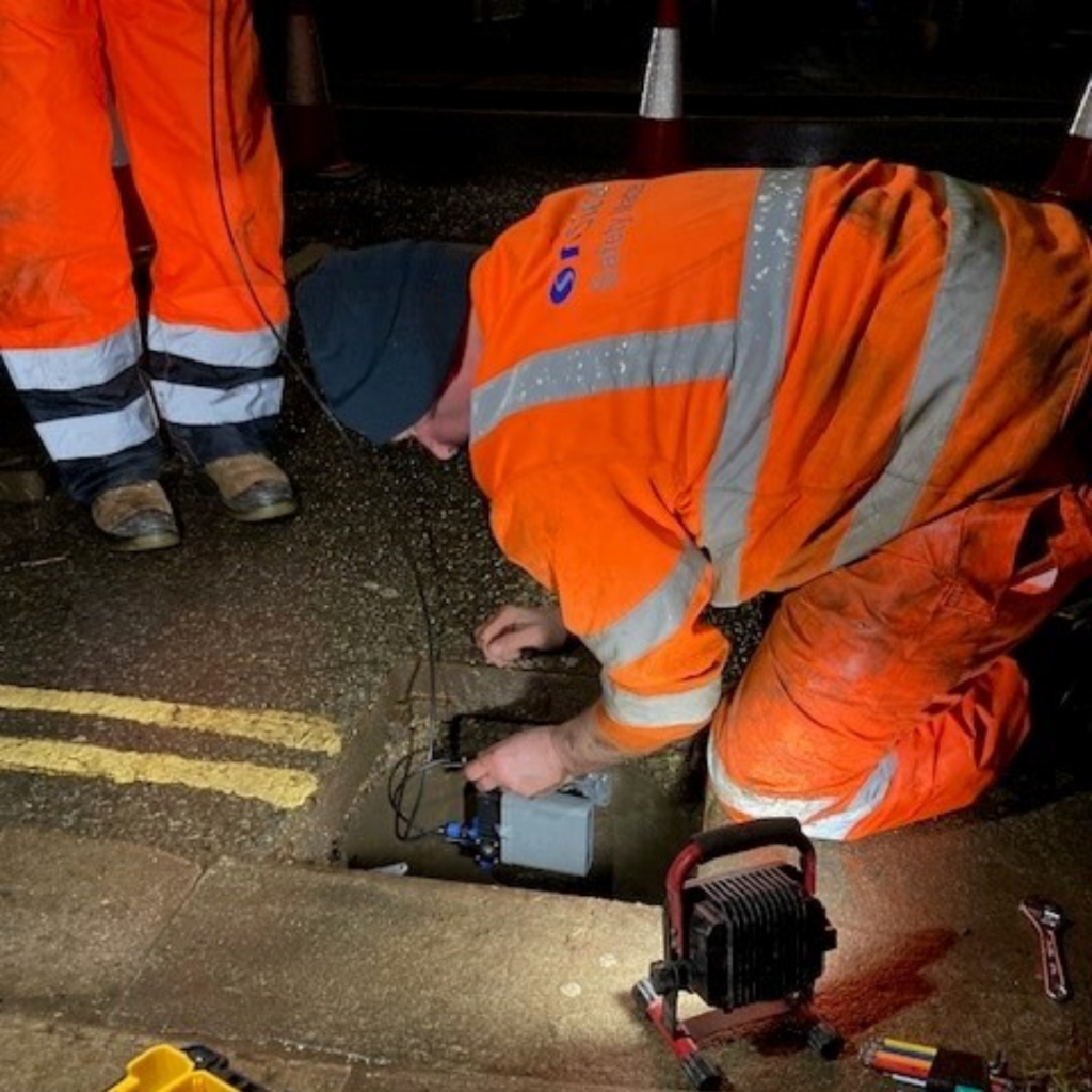 People in Hi vis installing a device into a gully