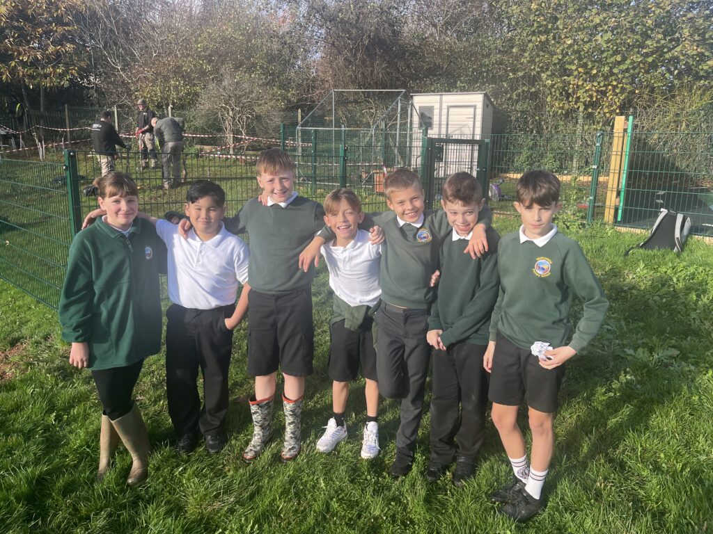 Smiling primary school pupils in uniform standing in a line on a grassy area outdoors.