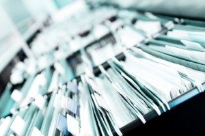 Multiple rows of filing cabinets in an office or medical establishment, overflowing with files. Narrow depth of field to emphasize the "neverending" feeling