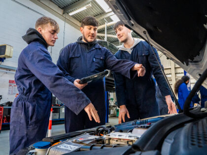Three young men in overalls are working on an electic vehicle as part of their t-level at South Devon College.