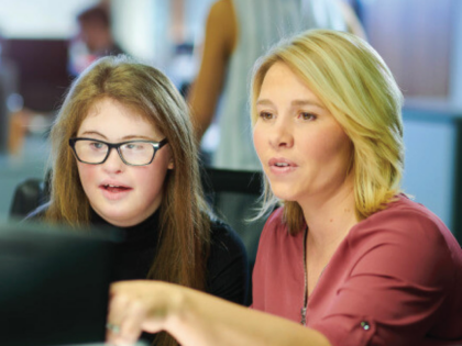 a young school leaver gets training on the computer in a busy office
