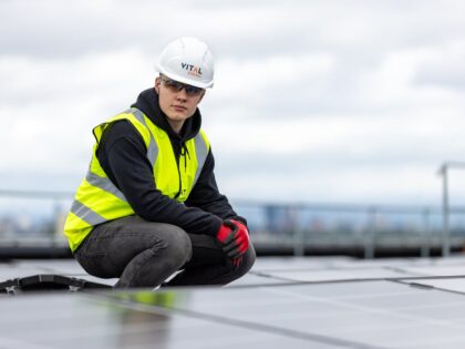 Man wearing a hi vis jacket and hard hat surrounded by solar panels