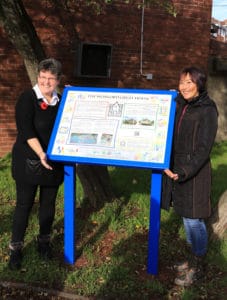 Two community members standing either side of The Wonford Great House information panel