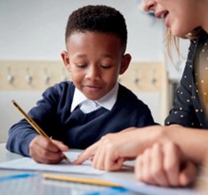 Young boy writing at a desk with an adult
