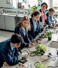 Children in a class room looking into microscopes with a teacher