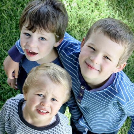 three boys smiling at the camera standing on grass