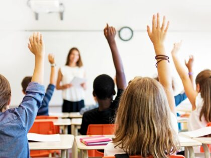 school pupils putting their hand up in a classroom with the teacher stood at the front