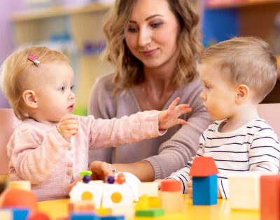 a nursery worker and two young children playing with blocks