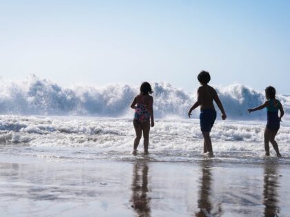 three children playing on the beach in front of a wave