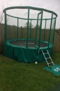 A photograph of the trampoline in the garden at Hillcrest; with a small ladder to help children climb up onto the trampoline, and netting surrounding the bouncing area to help keep users safe.