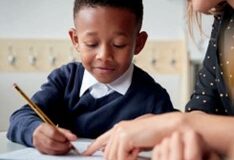 Young boy writing at a desk with an adult