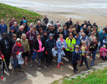 Group of about 40 people of various ages, probably litter picking by sea