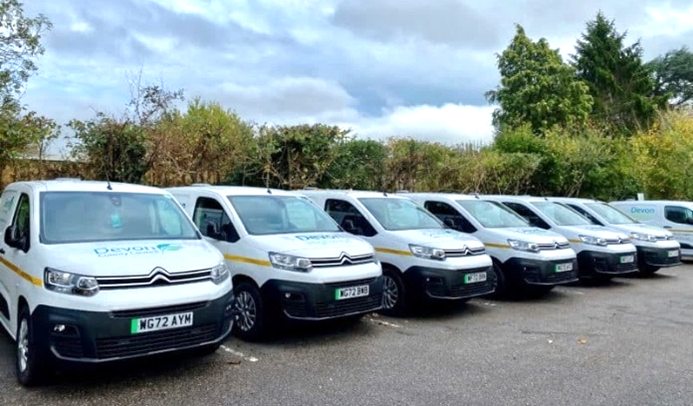 Row of electric fleet vehicles, white vans, in car park.