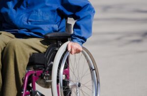 A person sitting in a wheelchair, with their left hand on the left wheel