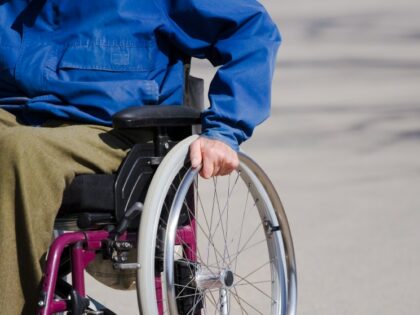 A person sitting in a wheelchair, with their left hand on the left wheel