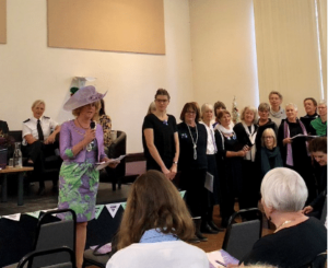 The Chair of County Council, Caroline Chugg opening the Vote 100 event. She is standing holding a microphone, addressing a group of people attending the event.