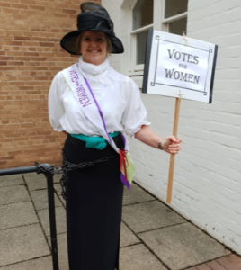 Picture of Suffragette Sue with 'votes for women' sign, chained to a railing at County Hall