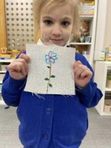 A girl proudly holds up her flower cross stitch.