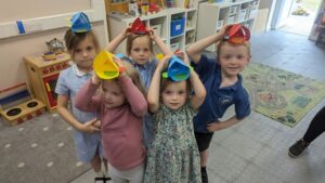 A group of 5 children in a childcare setting they have paper hats on their heads.