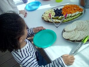 A child at the table with a plate of colourful fruit in front of them.